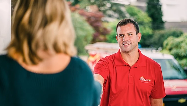 Smiling male handyman in red shirt greeting customer at their front door.