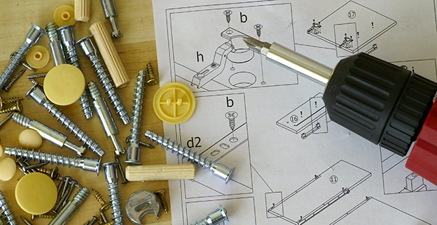 A collection of screws, wooden dowels, and tools scattered around assembly instructions for a furniture piece.