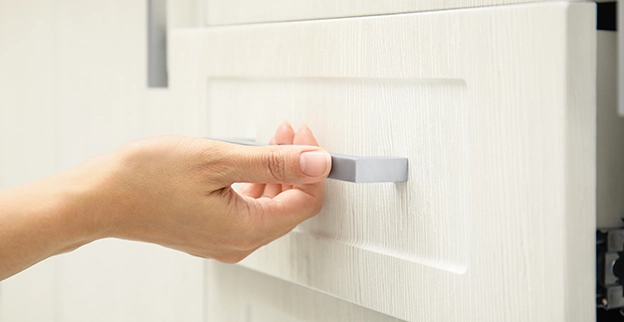 A hand reaching for a sleek, gray handle on a light-colored kitchen drawer.