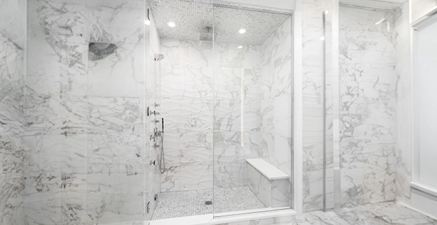 Spacious marble shower with glass wall featuring modern fixtures and overhead lighting.
