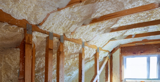 Interior of an attic featuring wooden beams insulated with white spray foam.