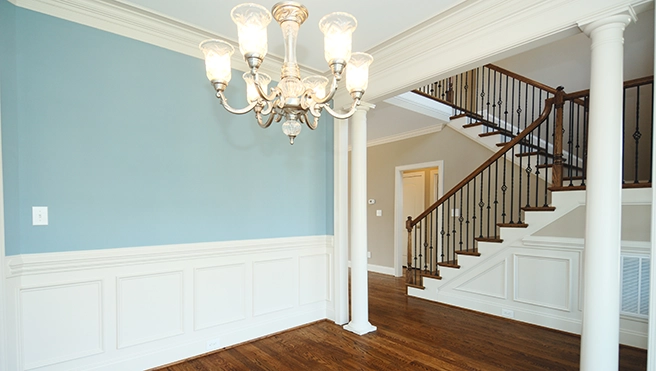 Elegant foyer featuring a decorative chandelier, blue wall, and a staircase with wooden railings and wainscoting accents.