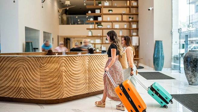 Two women with suitcases enter a modern hotel lobby.