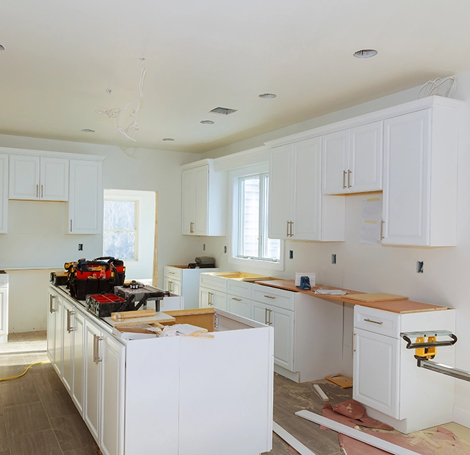 A partially renovated kitchen with white cabinets, exposed walls and tools scattered on the floor.