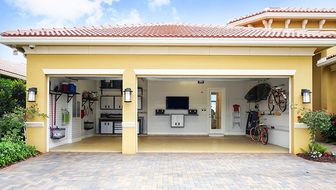 Spacious garage with organized shelving, tools, bicycles, and a TV, featuring a bright yellow exterior and a paved driveway.