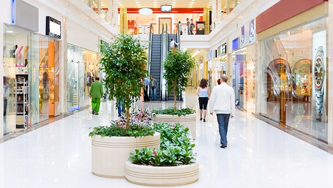 A shopping mall featuring escalators and shoppers browsing various stores along the sleek polished floor.